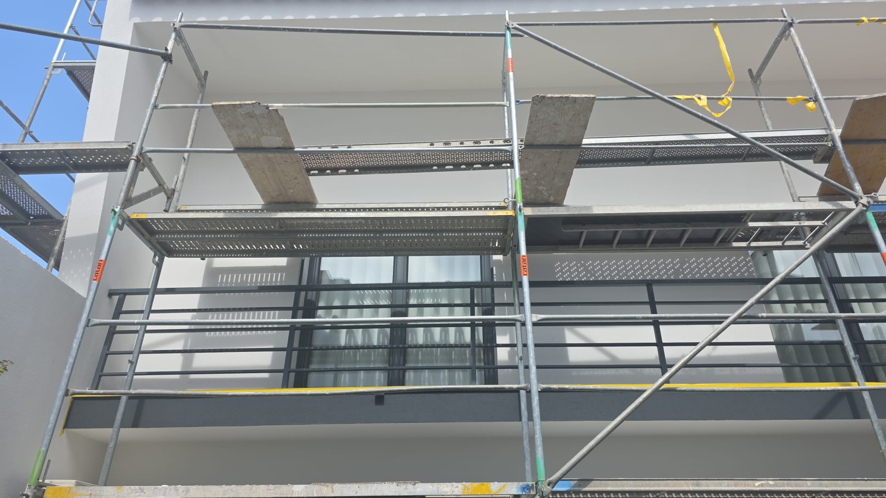Fachada de moradia em andaime durante o acabamento de pintura, com varanda e guarda em ferro