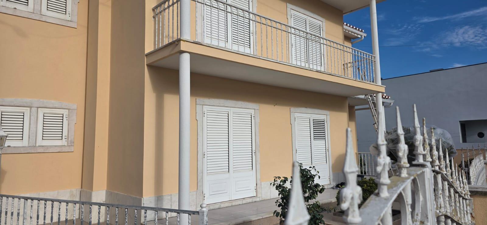 Fachada frontal de moradia bifamiliar após protecção e pintura em cor pêssego, com balcão e portadas em bom estado